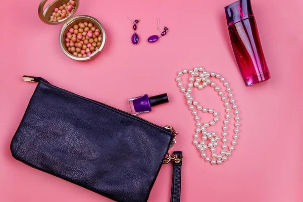 Clutch bag, pearl necklace, earrings, nail polish, rouge balls and bottle of perfume on pink background. Beauty and fashion concept. Flat lay, top view