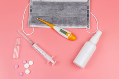 Koronavirüsü önleme ve tedavi etme kavramı. Tıbbi maske, el dezenfektanı, elektronik termometre, haplar, şırınga, pembe arka planda ampuller. Üst görünüm