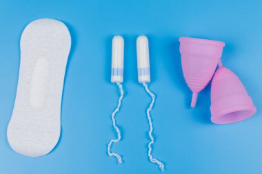 Mavi arka planda hijyenik ped, tampon ve regl kupası. Üst Manzara. Kritik günler, regl dönemi, kadın hijyeni