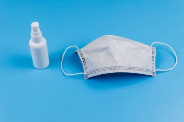 Mavi arka planda koruyucu tek kullanımlık tıbbi maske ve el dezenfektanı.