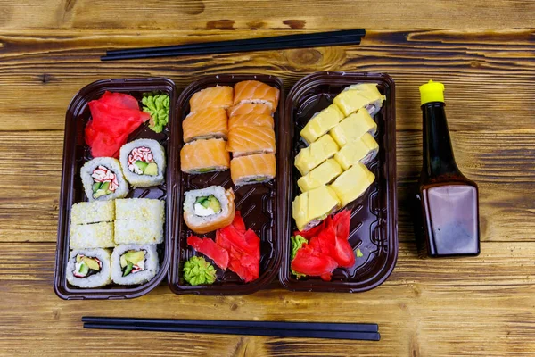 Set of sushi rolls in plastic boxes, soy sauce and chopsticks on wooden table. Top view. Sushi for take away or delivery of sushi in plastic containers