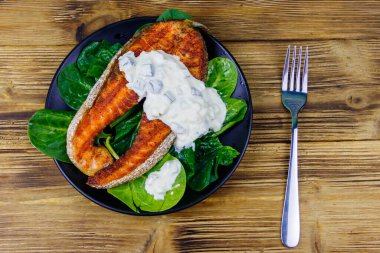 Ahşap masada ıspanaklı ve tartar soslu ızgara somon bifteği. Üst görünüm