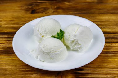 Tahta bir masada beyaz tabakta vanilyalı dondurma.