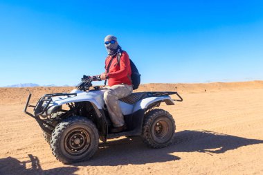 Safaride genç bir adam Mısır çölünde ATV kullanıyor. Hurghada, Mısır yakınlarındaki çölde dört tekerlekli bisiklet safarisi.