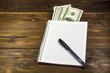 Tahta masanın üzerinde tükenmez kalem ve dolar banknotları olan defter. Para biriktirme kavramı