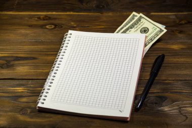 Tahta masanın üzerinde tükenmez kalem ve dolar banknotları olan defter. Para biriktirme kavramı
