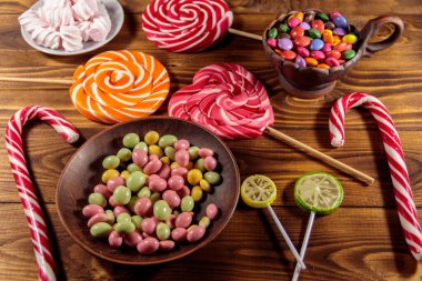 Renkli çikolata şekerlemeleri, lolipoplar, şeker kamışı ve marşmelovlar ahşap masada.