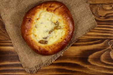 Ahşap masada süzme peynir ve kuru üzümlü (cheesecake) tatlı yuvarlak çörek. Üst görünüm