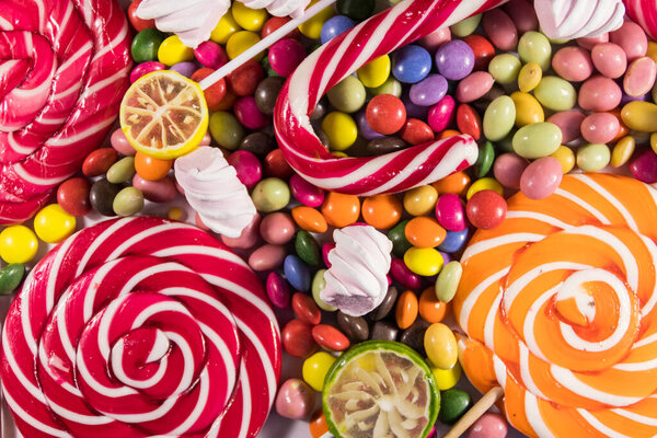 Background of colorful chocolate candies, lollipops, candy cane and marshmallows