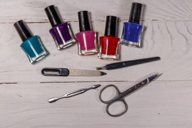 Beyaz ahşap arka planda temel manikür aletleri seti. Tırnak makası, tırnak makası, tırnak törpüsü ve oje şişeleri.