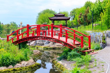 Japon bahçesindeki bir göletin yanında kırmızı köprü ve çardak.
