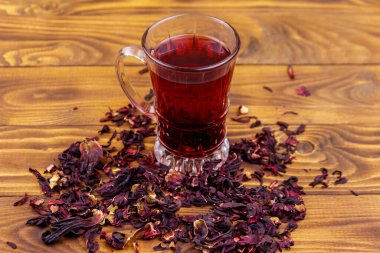 Ahşap masada bir bardak kırmızı amber çayı (carcade, roselle).