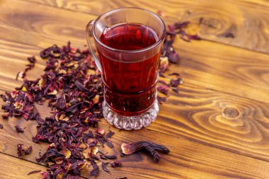 Ahşap masada bir bardak kırmızı amber çayı (carcade, roselle).