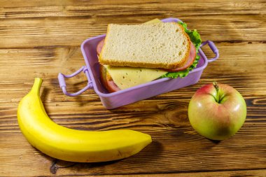 Sandviç, muz ve elmayla birlikte ahşap bir masada.