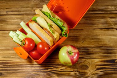 Elma ve beslenme çantası, sandviç ve taze sebzelerle ahşap bir masada. Üst görünüm