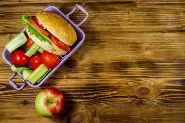 Elma, hamburger ve ahşap masada taze sebzeli beslenme çantası. Üst görünüm, alanı kopyala