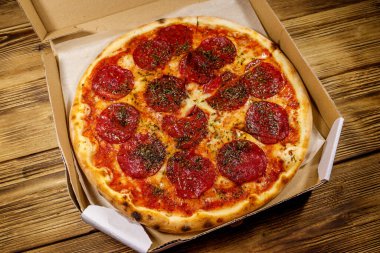 Tahta bir masanın üzerindeki karton kutuda nefis taze pizza. Yemek teslimatı, fast food, pizza teslimatı.