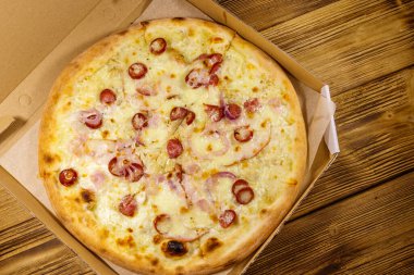 Tahta bir masanın üzerindeki karton kutuda nefis taze pizza. Üst Manzara. Yemek teslimatı, fast food, pizza teslimatı.