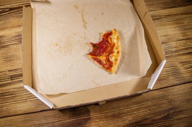 Tahta bir masadaki karton kutuda bir dilim pizza. Yemek teslimatı, fast food, pizza teslimatı.