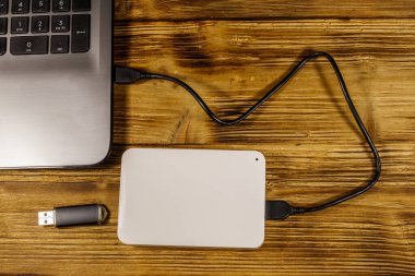 Harici HDD, tahta bir masadaki dizüstü bilgisayara ve USB flash diske bağlı. Üst Manzara. Veri depolama kavramı