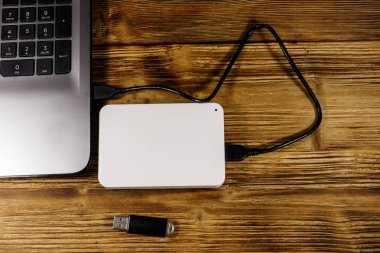 Harici HDD, tahta bir masadaki dizüstü bilgisayara ve USB flash diske bağlı. Üst Manzara. Veri depolama kavramı