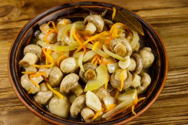 Tahta masadaki seramik kasede havuç, soğan ve baharatla marine edilmiş lezzetli mantarlar.