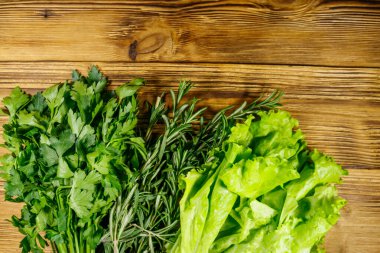 Taze yeşil maydanoz, marul yaprakları ve ahşap masada biberiye otları. Üst görünüm