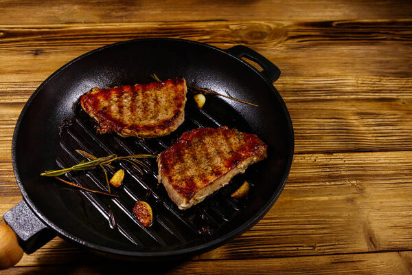 Grilled pork steaks with rosemary, garlic and spices in cast iron grill frying pan on wooden table