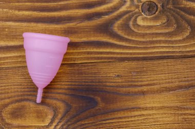 Ahşap arka planda tekrar kullanılabilen pembe silikon adet kupası. Üst görünüm, boşluğu kopyala. Kadın hijyeni, jinekoloji ve sağlık kavramı