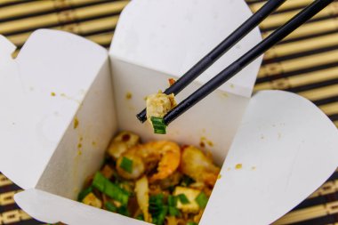 Kızarmış pirinç eriştesi, karidesli Pad Thai ve açık karton pakette tofu. Tayland mutfağı, yemek teslimatı.