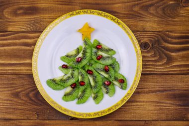 Tahta masada kivi dilimleri ve nar ağacından yapılmış Noel ağacı. Üst Manzara. Noel ve Yeni Yıl bayramı tatlıları için yaratıcı bir fikir. Çocuklar için komik yemek fikri.