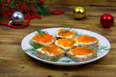 Kırmızı havyarlı kanepeler ve ahşap masadaki Noel süsleri.