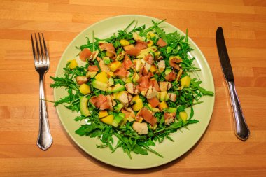 Tahta bir masada mango, avokado, somon, roka ve kızarmış ekmekle taze sağlıklı salata.