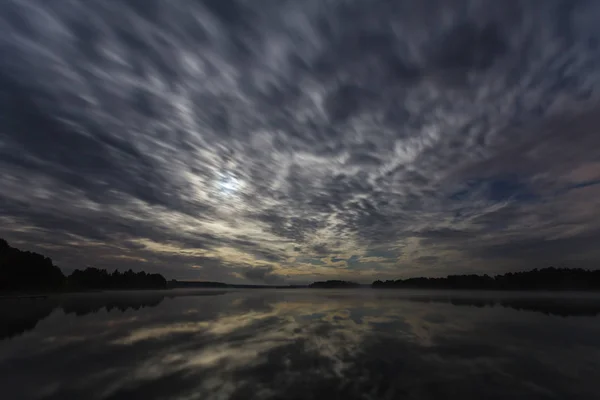Dynamic clouds in the night over the lake lit by full moon, long exposure shot