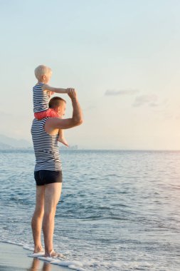 Baba oğlu deniz kenarında onun omuzlarında duruyor. Günbatımı zamanı