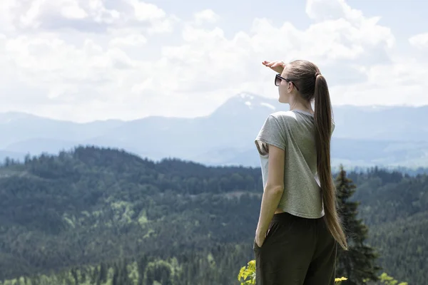 Women is standing and looking into the distance. Forest and mountains in the background