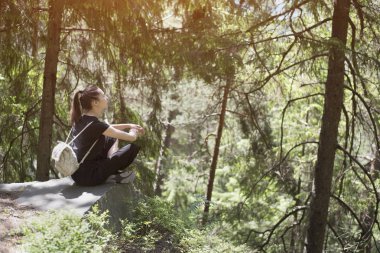 Sırt çantası ormandaki bir kayaya oturan kız. Yaz güneşli gün