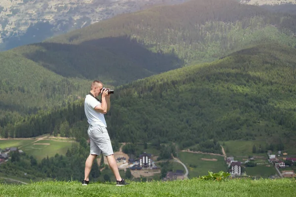 Man with camera standing on a hill and photography nature. Summer day
