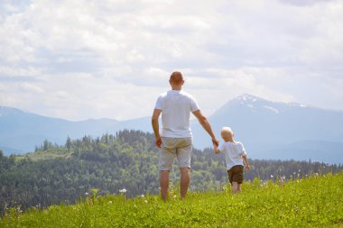 Çimenlerin üzerinde duran ve dağların hayran baba ve genç oğlu. Yaz güneşli gün. Arkadan görünüm