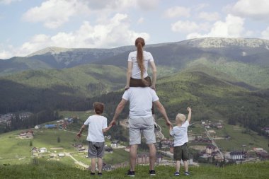 Aile iki oğlu ile dağlar arıyorum bir tepe üzerinde duruyor. Yaz günü. Arkadan görünüm.