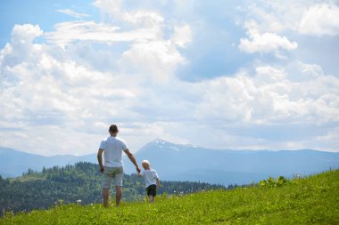 Çimenlerin üzerinde duran ve dağların hayran baba ve genç oğlu. Yaz güneşli gün. Arkadan görünüm