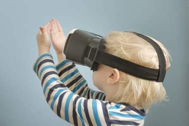 Sanal gerçeklik gözlüklü küçük sarışın çocuk. Ellerine bakar