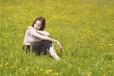 Düşünceli genç kadın bir çiçek çayır üzerinde oturur. Yaz güneşli gün