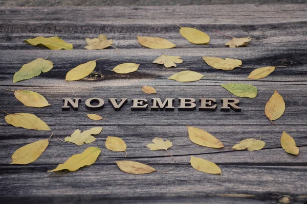 Ahşap arka plan üzerinde yazıt Kasım, çerçeve sarı yaprakları