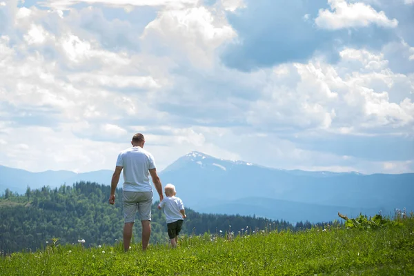 Çimenlerin üzerinde duran ve dağların hayran baba ve genç oğlu. Yaz güneşli gün. Arkadan görünüm