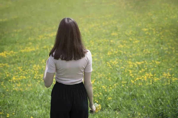 Genç kadın bir çiçek çayır üzerinde duruyor. Yaz güneşli gün. Arkadan görünüm