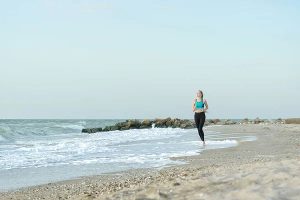 Girl in sportswear running along the surf line. Early morning.