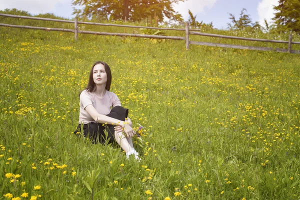 Düşünceli genç kadın bir çiçek çayır üzerinde oturur. Yaz güneşli gün