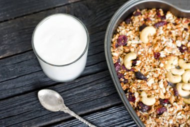 Bardak yoğurt ve bir fırın tepsisine kaju granola. Siyah ahşap masa