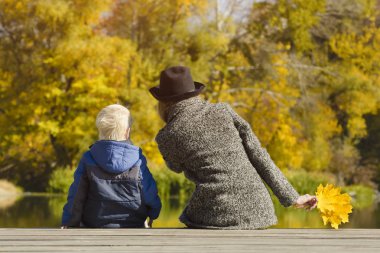 Sarışın çocuk ve annesi iskelede oturuyordu. Sonbahar günü. Arkadan görünüm